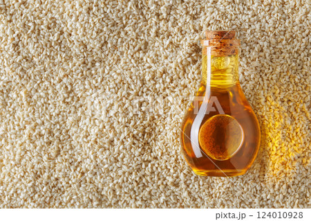 Glass bottle containing golden oil is placed on sesame seeds creating visually appealing contrast and showcasing the rich, essence of this versatile ingredient. Top view 124010928