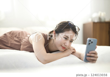 ベッドでくつろいでスマホを見る若い女性 ベッドでくつろいでスマホを見る若い女性 124013038