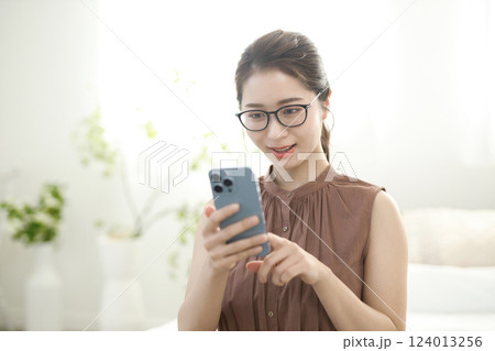ベッドに座ってスマホを見る若い女性 124013256