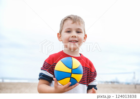 Young Boy Playing With a Colorful Beach Ball on a Sandy Shoreline During a Cloudy Afternoon Young Boy Playing With a Colorful Beach Ball on a Sandy Shoreline During a Cloudy Afternoon 124013838