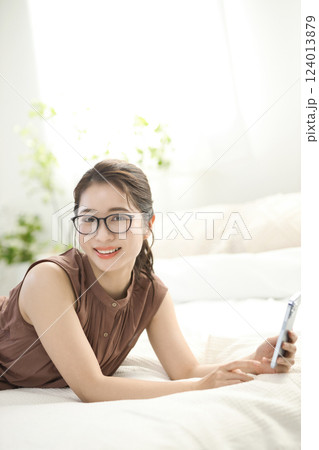 ベッドでくつろいでスマホを見る若い女性 124013879