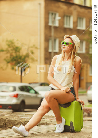 Woman traveler sits on suitcase waiting for car. 124015749