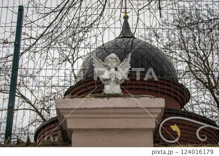 White figurine of an angel with wings. Statue of an angel on a fence column against the background of a church dome. 124016179