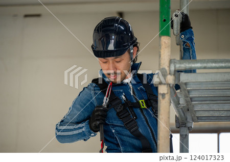 足場に安全帯をかけるヘルメットの男性 124017323
