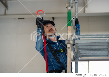足場に安全帯をかけるヘルメットの男性 124017324