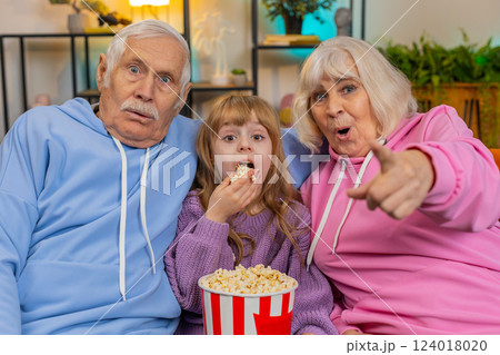 Child girl granddaughter grandfather grandmother eating popcorn watching movie film on home sofa Child girl granddaughter grandfather grandmother eating popcorn watching movie film on home sofa 124018020