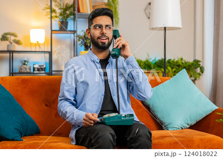 Indian man making retro wired telephone conversation talking with friends sitting at home couch 124018022