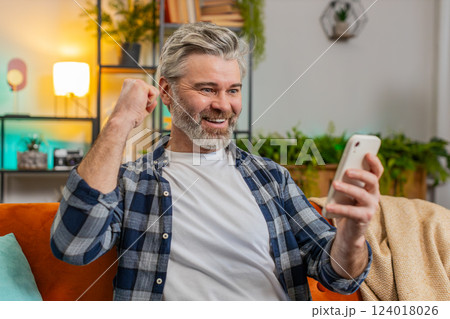 Surprised excited mature man winner holding smartphone reading good news amazed by online game win 124018026