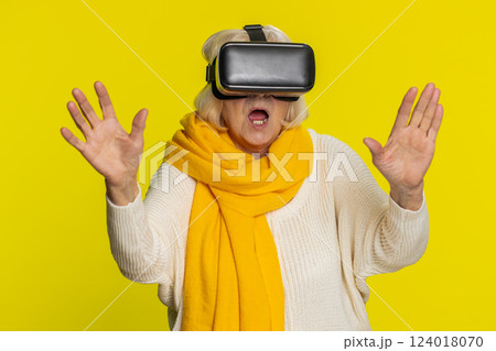 Senior woman in VR headset helmet watching virtual reality 3D video, playing simulation online game 124018070