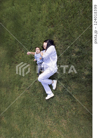 Asian smiling mom and sweet daughter are lying on a green lawn. A charming Korean woman and her cute kid are having fun on the grass. Asian smiling mom and sweet daughter are lying on a green lawn. A charming Korean woman and her cute kid are having fun on the grass. 124018399