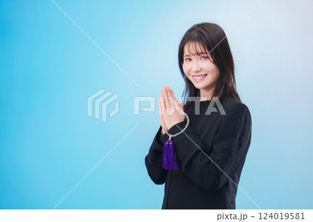 喪服を着て手を合わせる女性（水色背景） 124019581