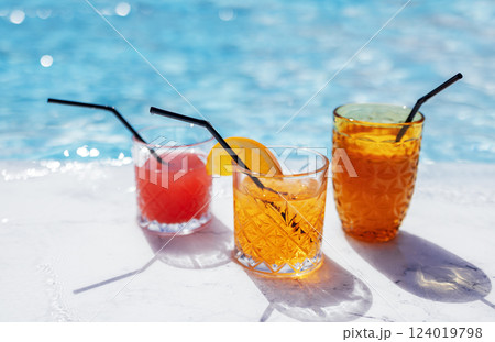 Close-up of three glasses with delicious cool cocktails by the pool. Cups with tasty fresh fruit juices on a background of blue water. Close-up of three glasses with delicious cool cocktails by the pool. Cups with tasty fresh fruit juices on a background of blue water. 124019798