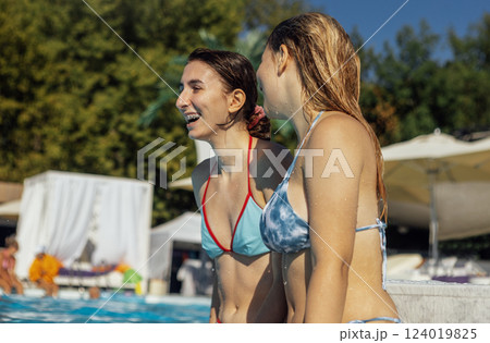 Two charming female friends are having fun in the pool. Smiling teenagers in swimsuits enjoy relaxing in the clear water. 124019825