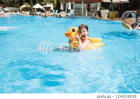 A little girl with an inflatable circle in the shape of a duck jumps into the pool. 124019838