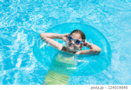 A little girl with an inflatable circle jumped into the pool. A cute kid in a swimsuit and swimming glasse 124019840