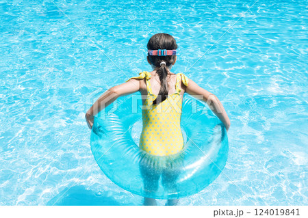 A little girl with an inflatable circle jumped into the pool. A cute kid in a swimsuit A little girl with an inflatable circle jumped into the pool. A cute kid in a swimsuit 124019841
