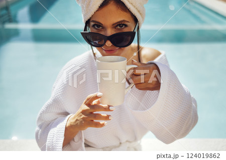 Young pretty woman in a white bathrobe holds a cup of coffee. Young pretty woman in a white bathrobe holds a cup of coffee. 124019862