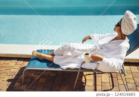 Young pretty woman in a white bathrobe lies on a sun lounger and holds a cup of coffee. 124019865