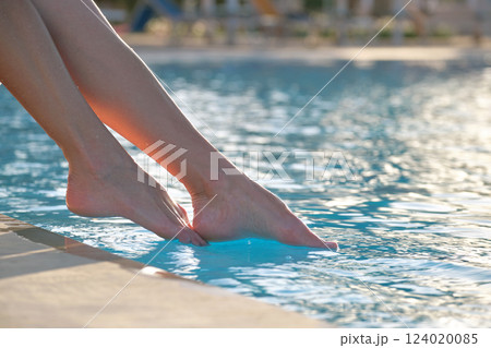 Young slim woman's legs relaxing near swimming pool in summer sun. Tropical vacation concept Young slim woman's legs relaxing near swimming pool in summer sun. Tropical vacation concept 124020085