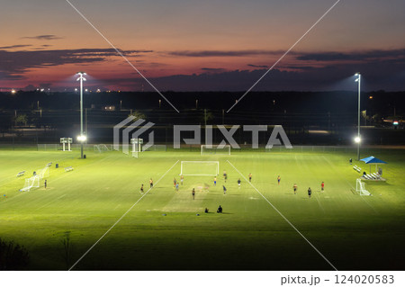 Sportsmen playing football game on illuminated stadium in public sports park 124020583