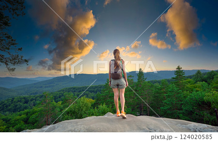 Sportive woman standing alone on hillside trail. Female hiker enjoying view of evening nature from rocky cliff on wilderness path. Active lifestyle concept 124020585