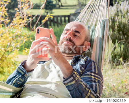 Man relaxing in hammock using smartphone outdoors 124020829