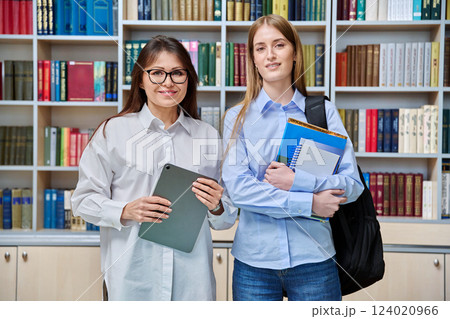 Portrait of middle aged female teacher and teenage girl student looking at camera in college library Portrait of middle aged female teacher and teenage girl student looking at camera in college library 124020966