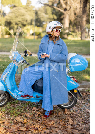 Elegant Woman Checking Phone Near Scooter in Park 124022255