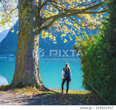 Young woman with backpack under a tree with yellow leaves, lake 124022447