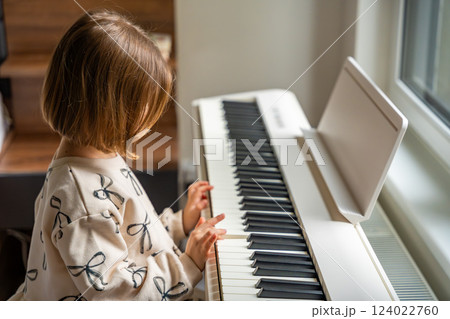 Home lesson on music for the girl on white piano synthesizer. Concept of early development: learning music enhances motor skills, hearing, and intelligence, fostering creativity from childhood 124022760