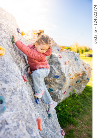 Little girl climbing an artificial climbing wall in a playground, developing strength and coordination Little girl climbing an artificial climbing wall in a playground, developing strength and coordination 124022774