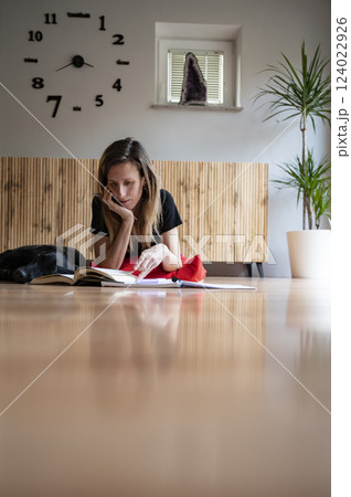 Low angle view of a young woman lying on a living room floor reading a textbook Low angle view of a young woman lying on a living room floor reading a textbook 124022926