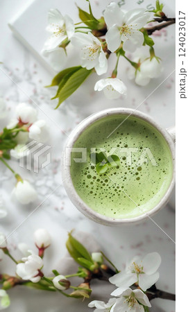 Delicate matcha drink topped with a heart-shaped leaf surrounded by white blossoms on a marble surface. Delicate matcha drink topped with a heart-shaped leaf surrounded by white blossoms on a marble surface. 124023017