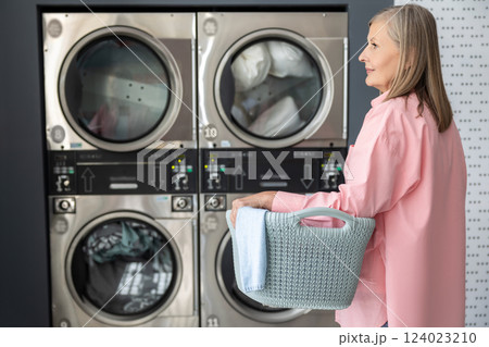 Senior woman washing clothes in laundromat using coin-operated machines for convenience Senior woman washing clothes in laundromat using coin-operated machines for convenience 124023210