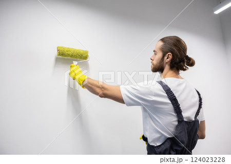 Dark-haired young bearded man in yellow gloves painting the wall 124023228