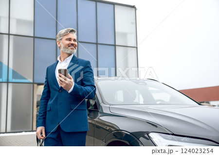 Businessman using his smartphone while standing at dealership 124023254