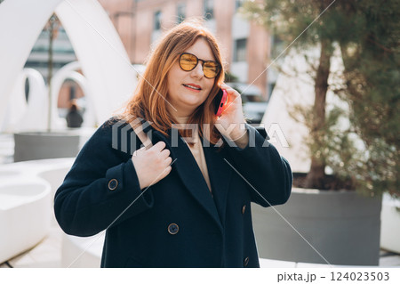 Happy 30s woman talking phone and look happy outdoors. Urban lifestyle concept. Spring time. Beautiful woman walking on the modern city street. Happy 30s woman talking phone and look happy outdoors. Urban lifestyle concept. Spring time. Beautiful woman walking on the modern city street. 124023503