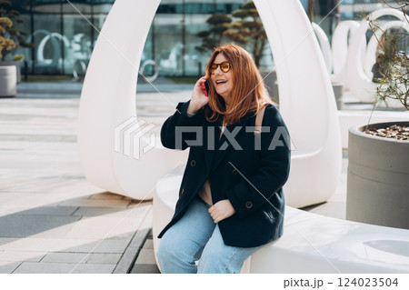 Happy 30s woman talking phone and look happy outdoors. Urban lifestyle concept. Spring time. Beautiful woman walking on the modern city street. 124023504