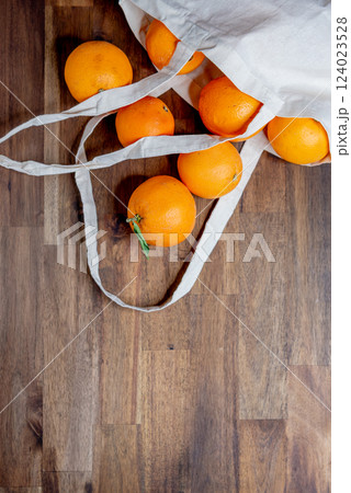 fresh unpeeled oranges placed in reusable nature textile bag on brown table. fresh unpeeled oranges placed in reusable nature textile bag on brown table. 124023528