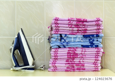 Ironing linen with steam generator. A stack of ironed towels lying next to the iron. Teflon sole plate covered with small holes. 124023676