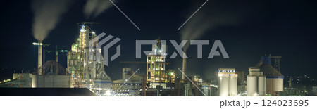 Illuminated cement plant with high factory structure and tower cranes at industrial production area at night. Manufacture and global industry concept 124023695