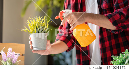 Young man watering a potted plant with a spray bottle in a contemporary indoor garden Young man watering a potted plant with a spray bottle in a contemporary indoor garden 124024171