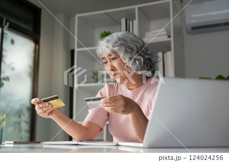 Concerned senior woman comparing credit cards while shopping online at home Concerned senior woman comparing credit cards while shopping online at home 124024256