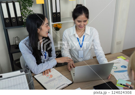Diverse business team reviewing reports and analyzing data on a laptop in a meeting. 124024308