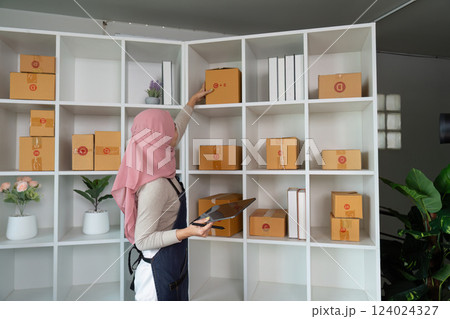 Muslim woman organizing packages on a shelf in her home office for online sales. Muslim woman organizing packages on a shelf in her home office for online sales. 124024327