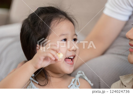 Joyful Childhood Moments and Snack Time. A little girl excitedly enjoys popcorn while interacting with a family member. 124024736