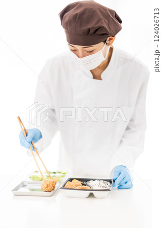 惣菜を弁当に盛り付けるマスク姿の女性 124026713