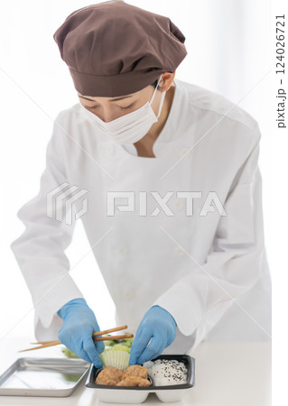 惣菜を弁当に盛り付けるマスク姿の女性 124026721