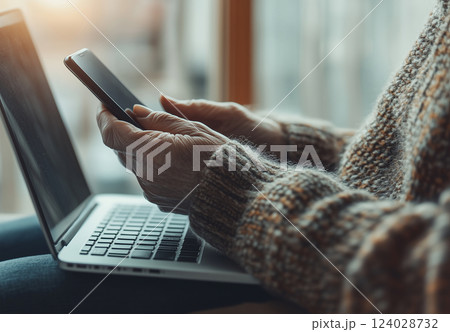 PCの前でスマートフォンを操作する高齢者の手元 PCの前でスマートフォンを操作する高齢者の手元 124028732