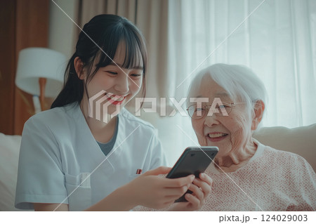 施設のスタッフにスマホ操作を教わるおばあちゃん 124029003